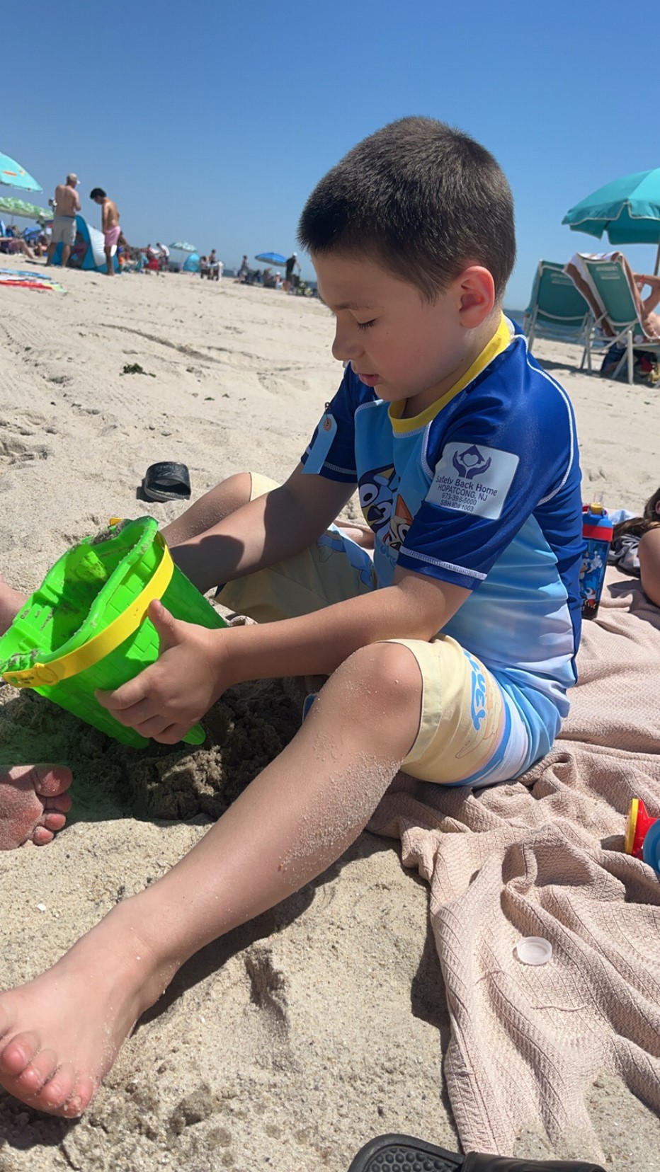 Xavier playing with a green bucket on a sandy beach.