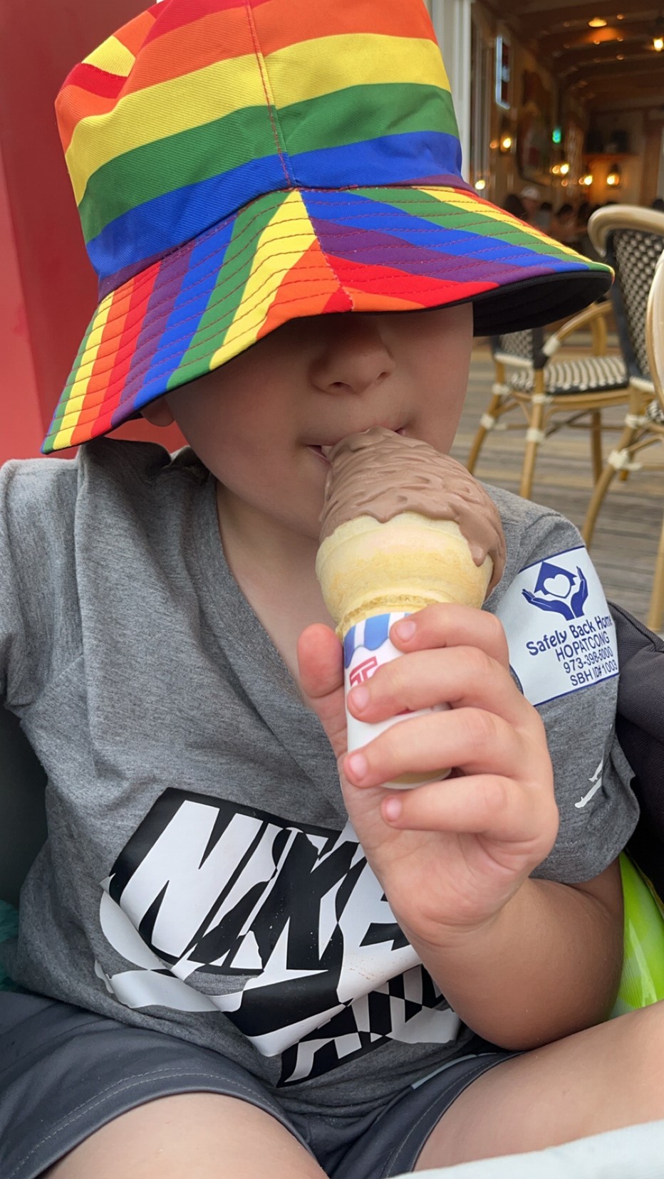 Xavier in a colorful rainbow hat enjoying an ice cream cone on a sunny day.